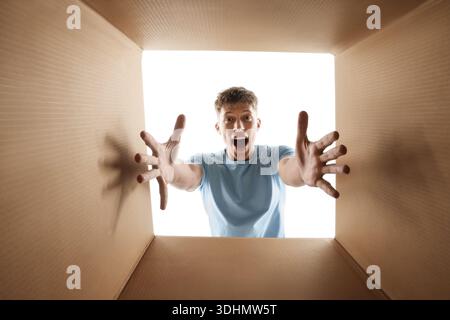 Man looking into cardboard box against white background, view from inside package Stock Photo