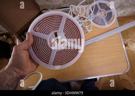 Top-down view of person's hand holding white reel of red LED lights near tangled wires on table Stock Photo
