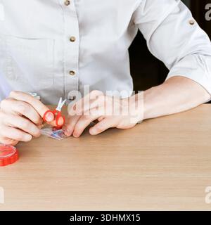 Close-up of male hands using small red scissors to cut open plastic packet with needles on table Stock Photo