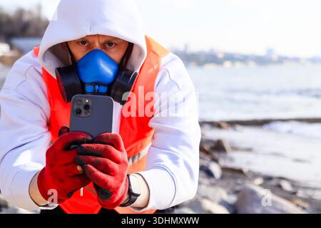 Close view of man in blue mask and red gloves using phone with reflective vest by blurry city. Stock Photo