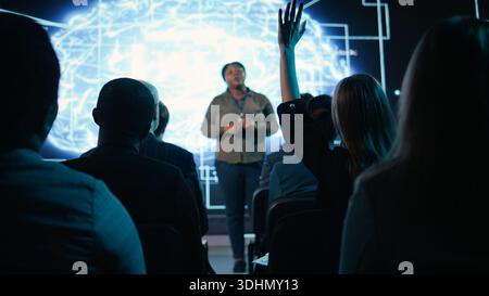 Girl in audience interacting with black female speaker presenting AI systems at business convention, showing automation and AI brain visuals for software development. Active participants. Stock Photo