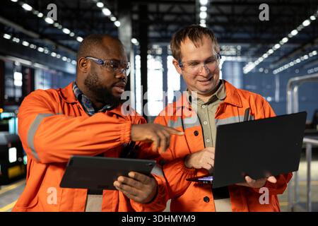 Diverse personnel using gadgets for steel production tasks in factory, surrounded by metal machinery and fabrication tools. Engineering and efficient manpower on the factory floor. Stock Photo