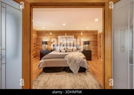 Modern staged bedroom interior with wood panel walls, neutral tones, and warm lighting, ideal for real estate, interior design, and lifestyle concepts Stock Photo