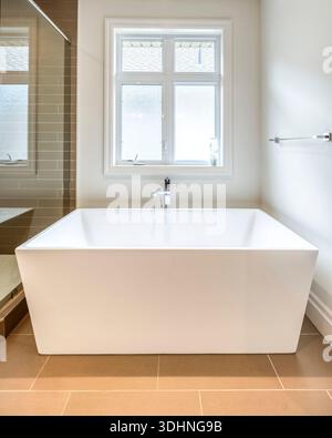 Modern minimalist bathroom with a freestanding white bathtub, neutral tones, and natural light, evoking luxury, calm, and contemporary interior design. Stock Photo