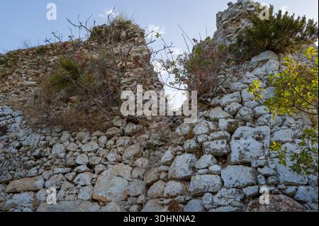 Peloponnese, Greece - September 6, 2024: A gap in the ruined stone wall of Navarino Castle is visible with overgrown shrubs and small trees growing among the stones under a clear sky. Stock Photo