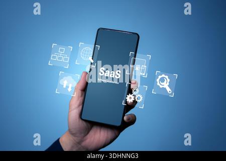 Hand holding smartphone showing SaaS software as a service with cloud, network and settings icons, representing mobile cloud apps, subscription platfo Stock Photo