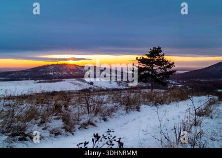 Sunset Over Snowy Hills With Lone Pine Tree And Open Field At Dusk Stock Photo