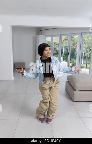 African American woman standing arms spread in living room sliding glass doors wearing denim jacket Stock Photo
