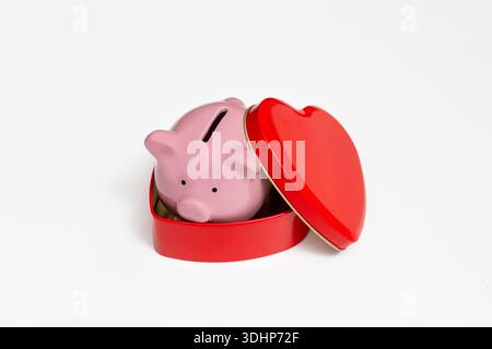 Piggy bank in a tin box of chocolates in the shape of a heart, white background, the concept of spending on gifts for Valentine's day Stock Photo