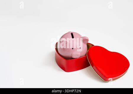 Piggy bank in a tin box of chocolates in the shape of a heart, white background, the concept of spending on gifts for Valentine's day Stock Photo