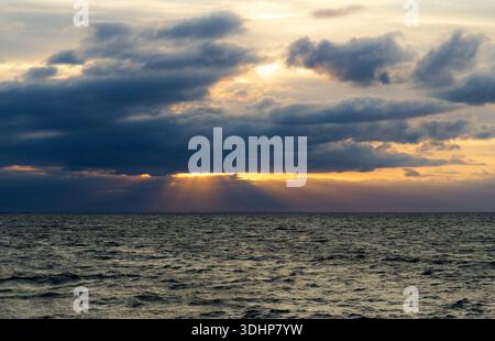 Dramatic seascape with sun rays breaking through dark storm clouds over the ocean Stock Photo