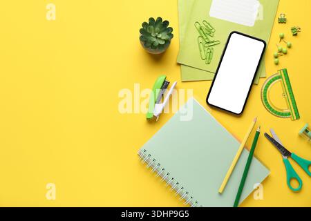 Set of school stationery with mobile phone and houseplant on yellow background Stock Photo