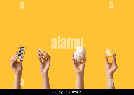Female hands holding mini deck chairs with seashells on yellow background Stock Photo