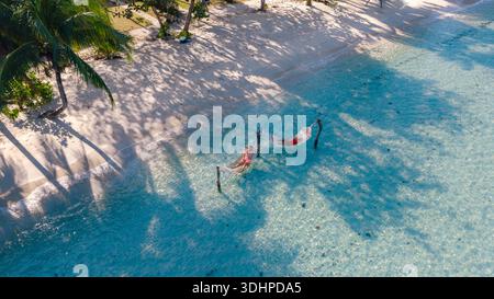 Two people enjoy a serene day in hammocks gently swaying above the turquoise waters of Bang Bao Beach, surrounded by palm trees and soft sandy shores Stock Photo