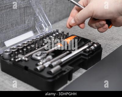 Close-up of a hand choosing a screwdriver from an open toolkit with various chrome socket wrenches and bits, perfect for DIY or professional repair Stock Photo
