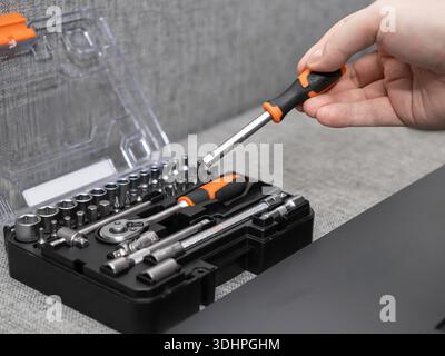 Close-up shot of a hand selecting an orange and black screwdriver from an organized professional repair toolkit, signifying meticulous readiness for v Stock Photo