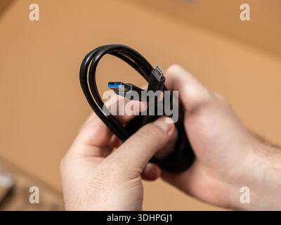 Close-up shot of hands holding a versatile black USB data cable, featuring both Type-A and Type-C ends for charging modern electronics and connecting Stock Photo