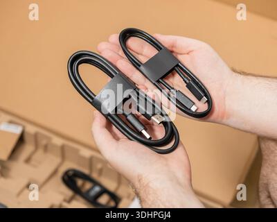 Close-up of hands presenting two essential black USB cables, including Type-C to Type-C and Type-A to Type-C connectors, ideal for unboxing new techno Stock Photo