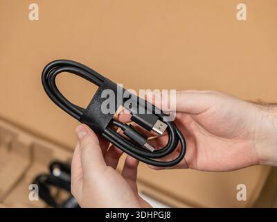 Close-up of male hands holding a coiled black USB-C to USB-A cable, signifying unboxing new electronics, essential data transfer, and charging solutio Stock Photo