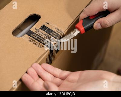 Close-up of a person's hand cutting tape on a brown cardboard delivery box using a utility knife for secure package opening and careful goods inspecti Stock Photo