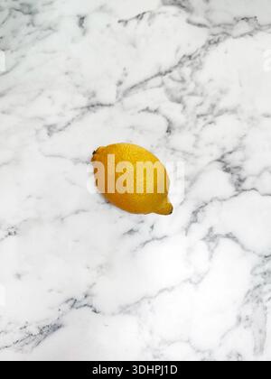 yellow ripe lemon with shiny peel lies alone on marble gray-white surface, citrus, fruit food, isolated object Stock Photo
