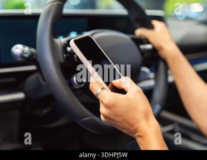 Close-up of smartphone in hand of woman behind steering wheel Stock Photo
