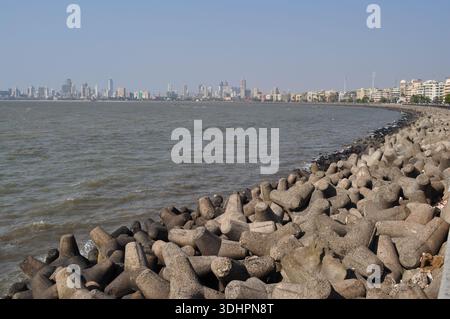 Coastal tetrapod sea defenses line the shoreline with the Mumbai skyline in the distance, India Stock Photo