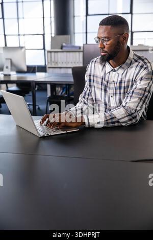 Mid-adult African American man working on silver laptop at matte-black office table wearing glasses Stock Photo