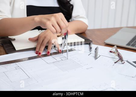 Female architect using dividers working on blueprint architects project in office. Stock Photo