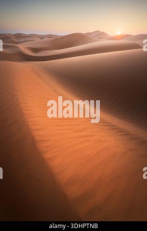 View of rippled sand dunes sweeping across the landscape under a soft sunrise, casting long shadows in the desert, Ubar, Dhofar Governorate, Oman. Stock Photo