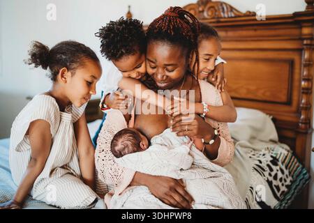 Black mom nursing multiracial newborn baby daughter and son hugging Stock Photo