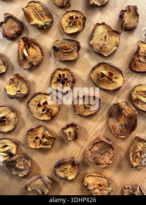 Flat lay of dried apple slices with visible seeds arranged on a natural wooden surface, forming an organic food texture background Stock Photo