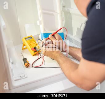 Close-up on an electrician fixing an electrical outlet of refrigerator and measuring the voltage. Stock Photo