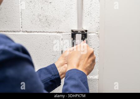 Electrician mounting electric sockets on the white wall. Electrician wiring a new build. Worker installing socket in new house. Man installing light s Stock Photo