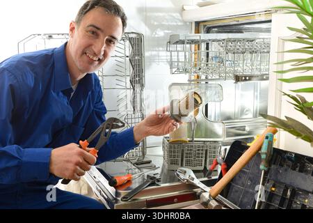 Detail of male technician specialist dressed as a blue working man doing maintenance on a dishwasher with tools around in a white kitchen Stock Photo