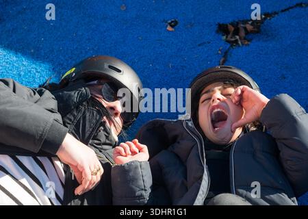 Mother and daughter wearing helmets lying on a blue ground, child making funny face Stock Photo