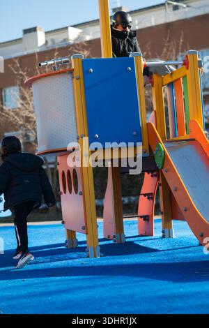 Children wearing helmets playing outdoors on a colorful playground Stock Photo