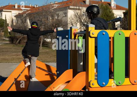 Two children wearing helmets having fun on a colorful playground structure Stock Photo