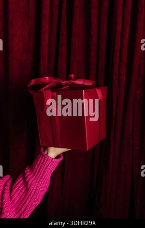 Woman holds red gift wrapped with red ribbon in hand Stock Photo