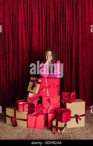 Woman smiles at camera while leaning on a stack of gifts Stock Photo