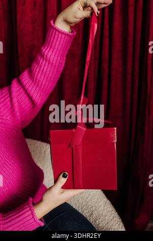 Close up of woman pulling on red bow to open a wrapped package Stock Photo