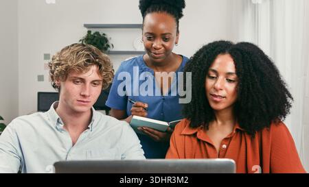 Diverse Trio Collaborating on Laptop in a Modern Startup Office Setting for Teamwork and Innovation Stock Photo