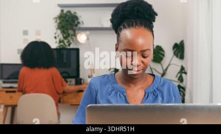 Focused Female Professional in Modern Office Working on Laptop Amid Collaborative Startup Team Environment Stock Photo