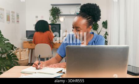 Young Professional Woman Working at Desk with Laptop and Notebook in Modern Office Stock Photo