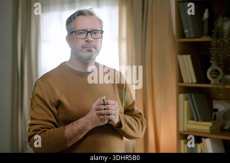 Portrait of Middle Aged Man Standing Indoors Holding Rosary Beads Stock Photo