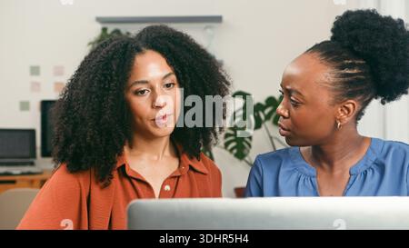Two Women Collaborating in a Modern Startup Office With Laptop and Focused Discussion Stock Photo