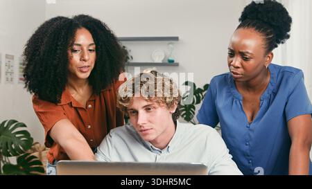 Diverse Startup Trio Collaborates Around Laptop in Modern Office Setting Stock Photo