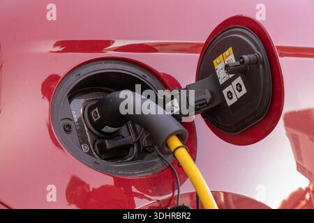 Close-up of a European Type 2 electric vehicle charging port (Mennekes) integrated into a red car, with a yellow AC charging cable connected, highligh Stock Photo