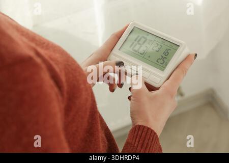 Woman Adjusting Programmable Thermostat for Home Heating and Cooling Control, Close Up Stock Photo