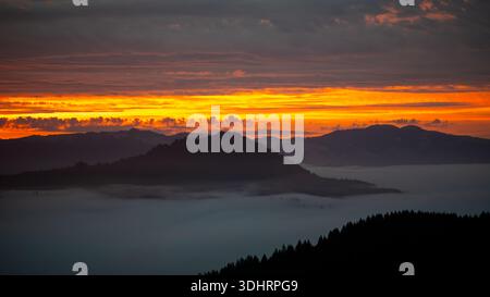 View of the tranquil landscape with fog nestled between the dark silhouettes of rolling hills beneath a vibrant sunset, Salmon Creek, California, Unit Stock Photo